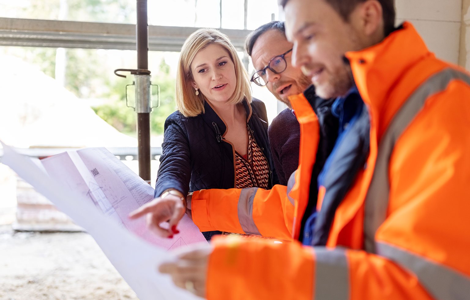 Personen besprechen Baupläne auf einer Baustelle.