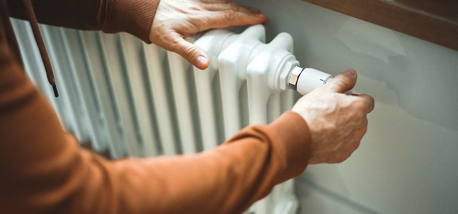 Eine Person stellt das Thermostat an einem Heizkörper ein.