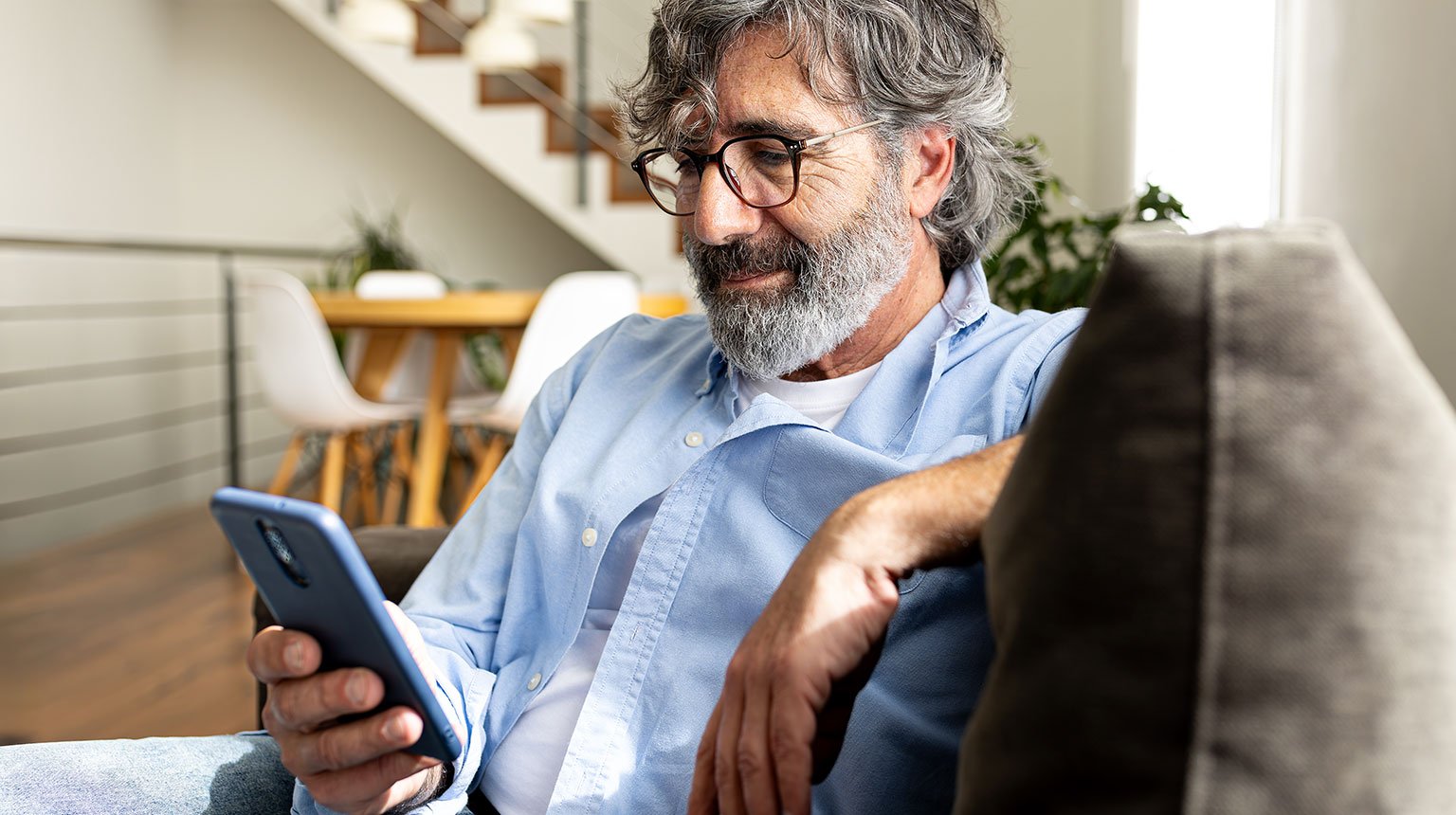 Ein Mann sitzt auf dem Sofa und schaut auf sein Smartphone.