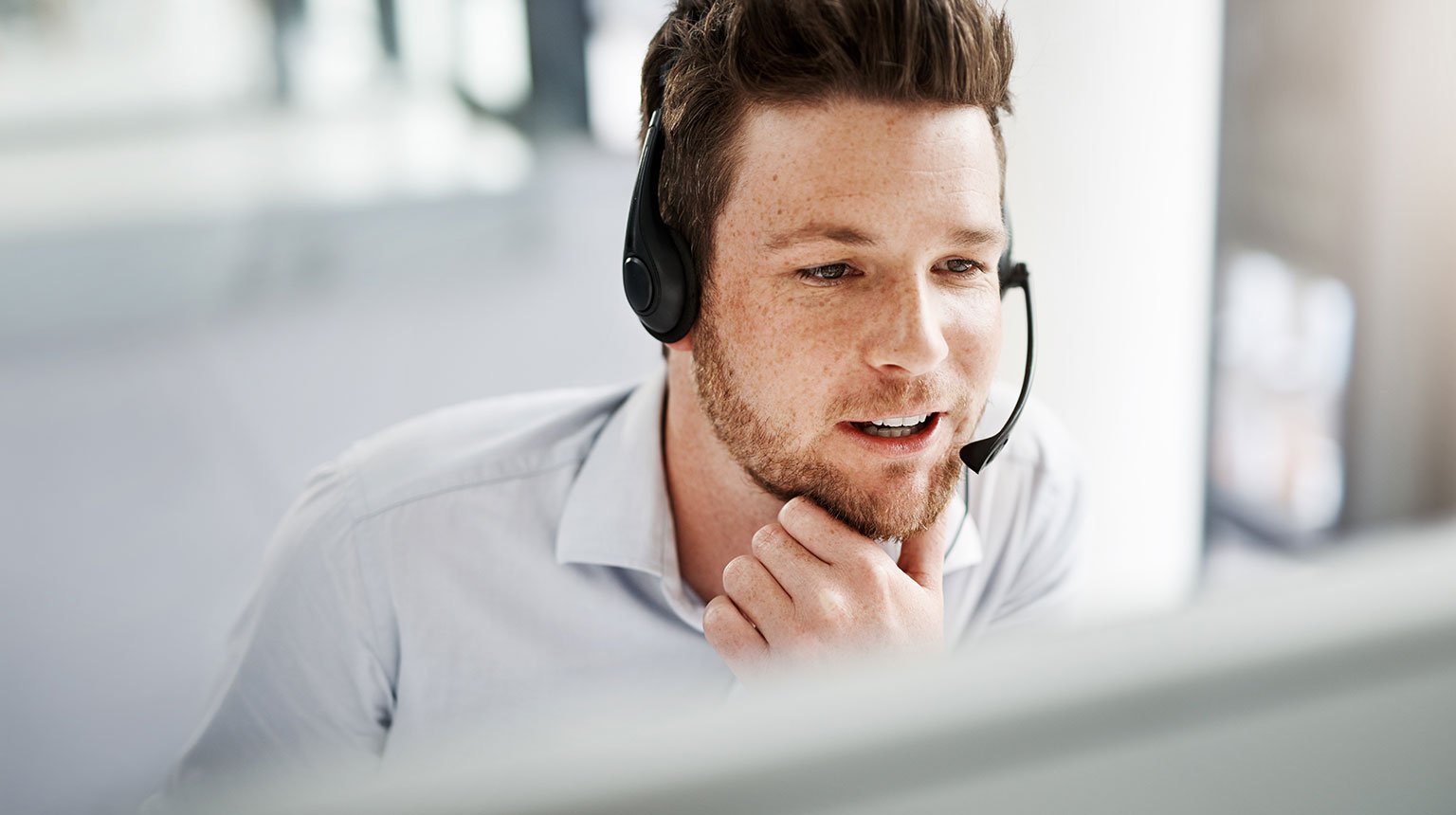 Mitarbeiter im Kundendienst mit Headset vor dem Bildschirm.