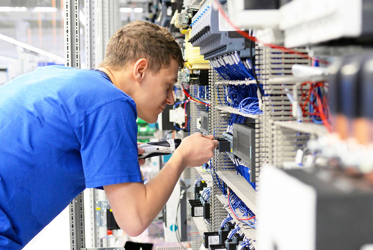 Junger Mann arbeitet konzentriert an einer Schalttafel mit vielen Kabeln in der Werkstatt.