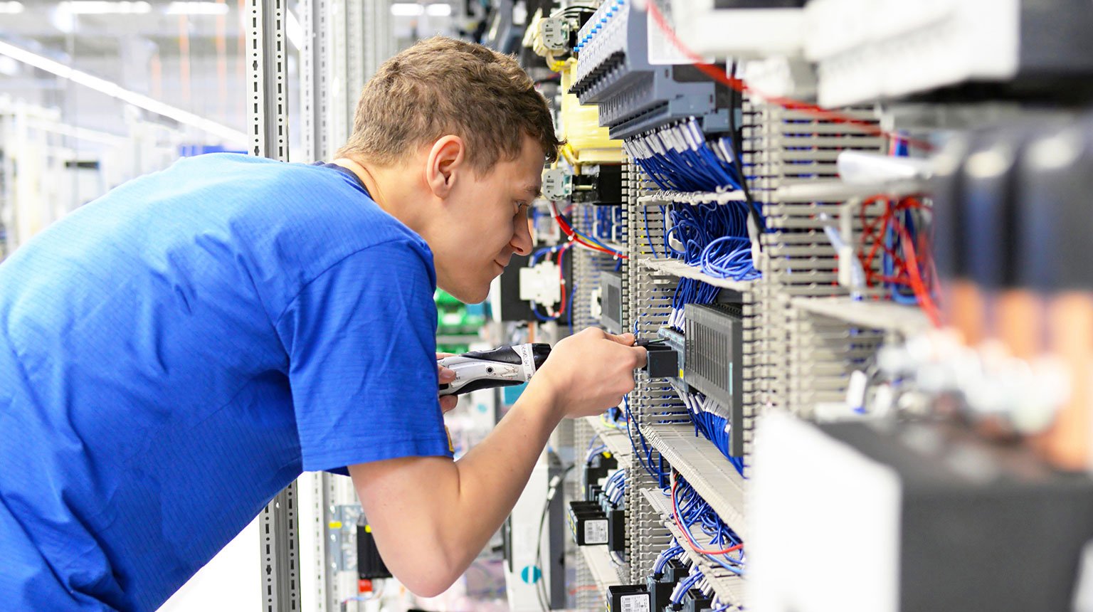 Junger Mann arbeitet konzentriert an einer Schalttafel mit vielen Kabeln in der Werkstatt.