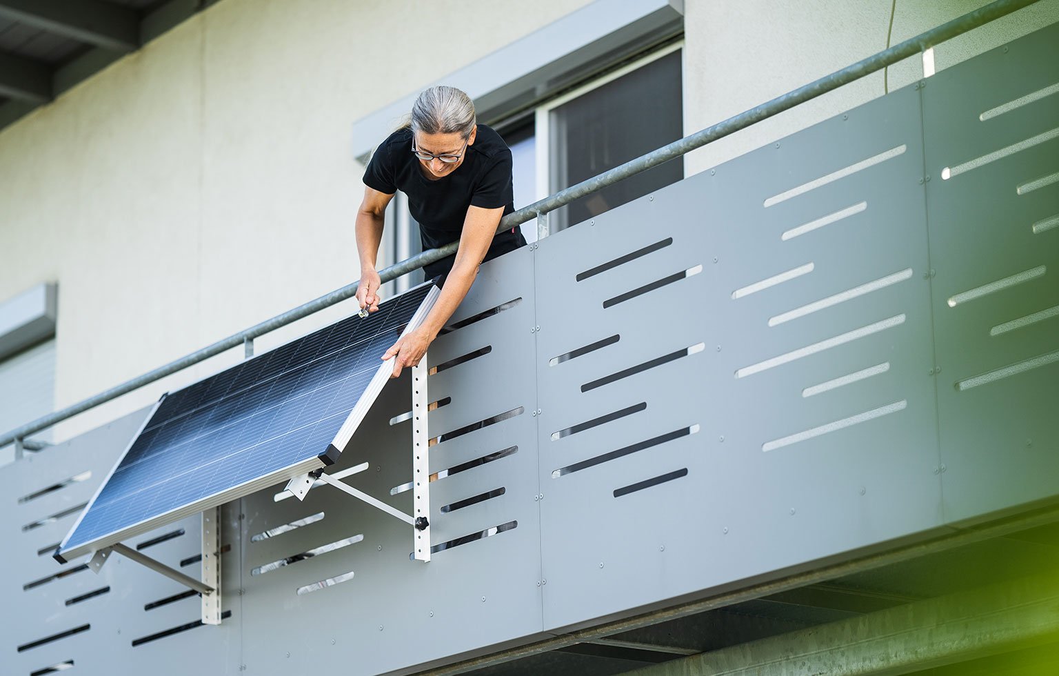 Person montiert ein Balkonkraftwerk am Geländer ihres Wohnungsbalkons.