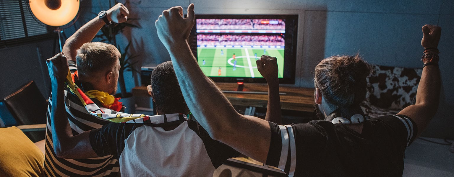 Drei Fussballfans jubeln gemeinsam vor dem Fernseher.