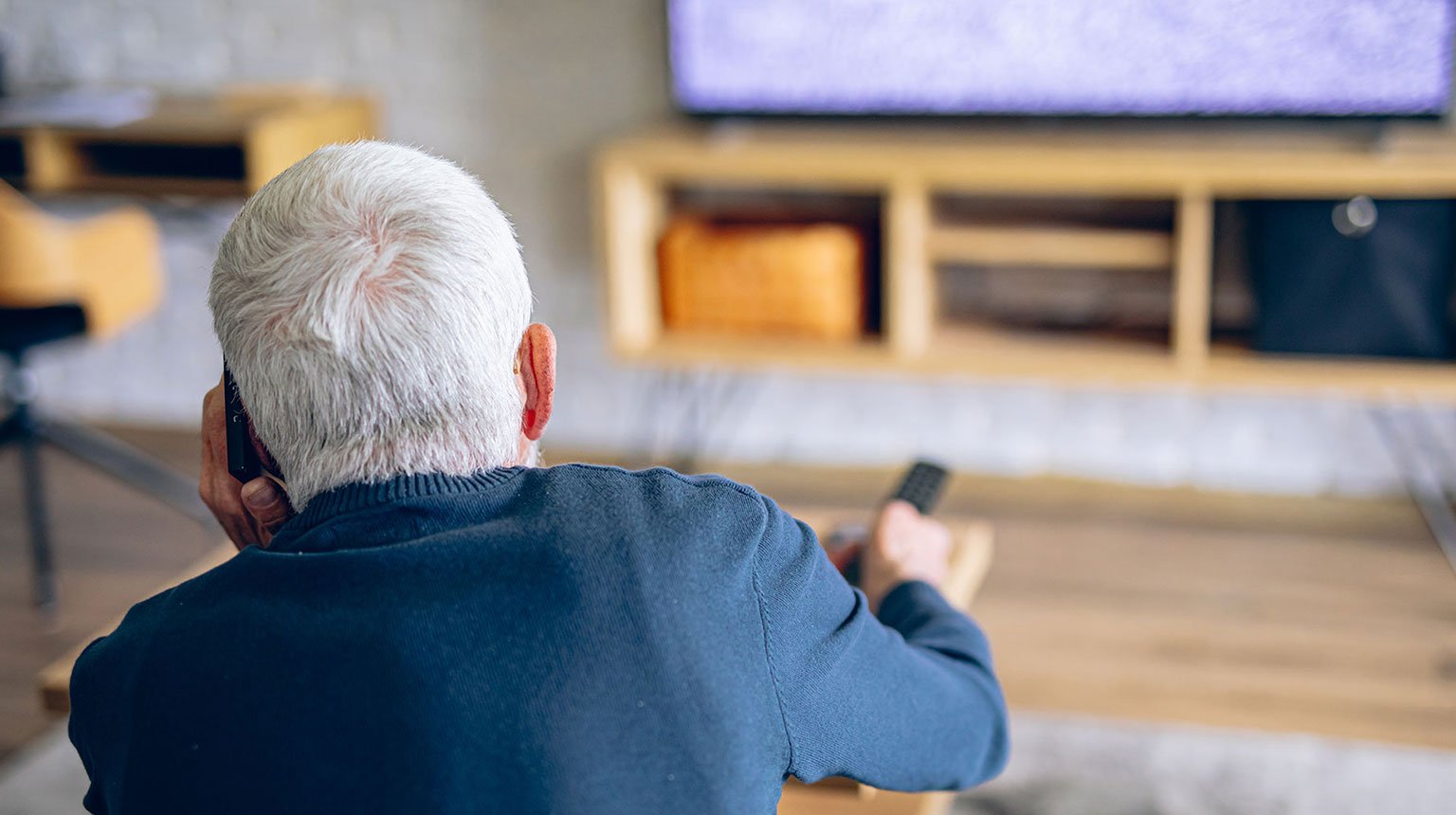 Ein älterer Mann telefoniert mit dem Kundendienst, während der Fernseher kein Signal zeigt.