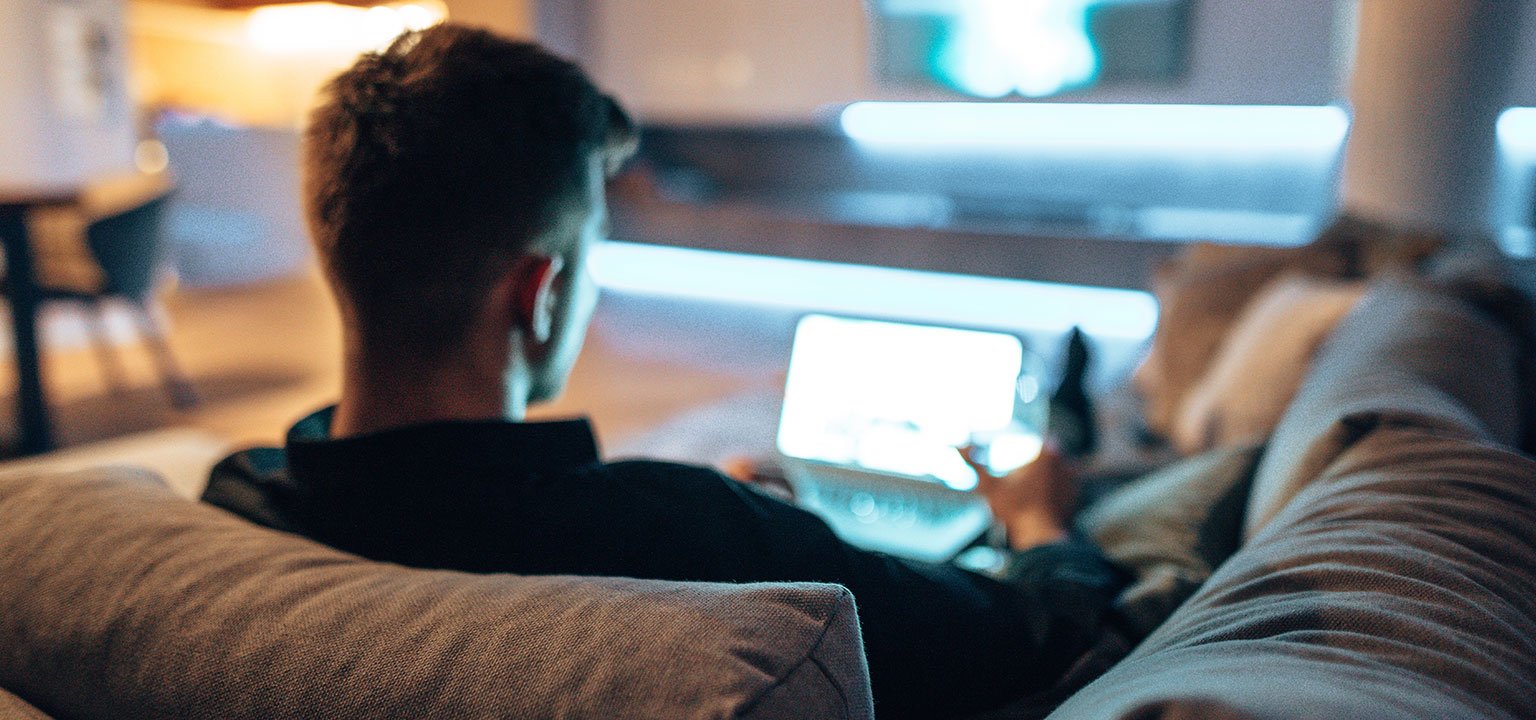 Ein Mann sitzt entspannt auf dem Sofa und nutzt ein Tablet.