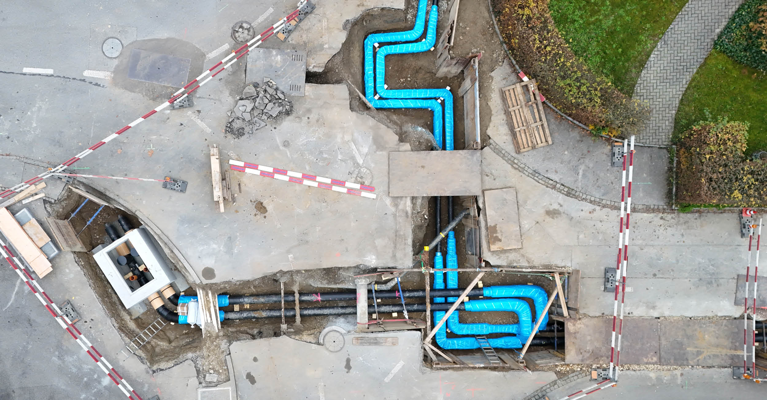 Luftaufnahme einer Strassenbaustelle mit neu verlegten, blau isolierten Fernwärmeleitungen.