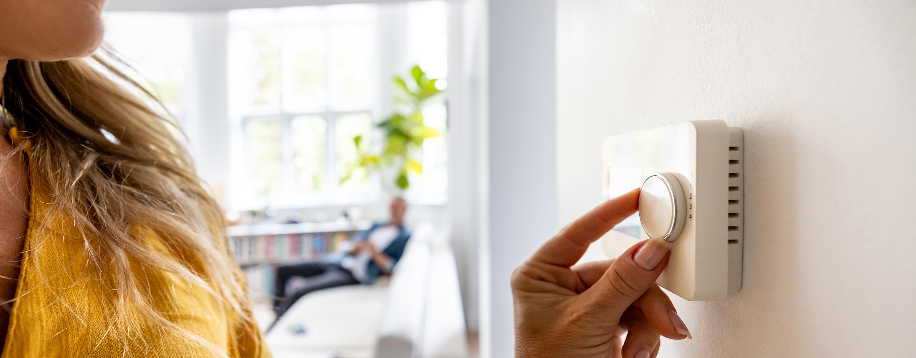 Frau regelt die Temperatur an einem Wandthermostat in einem hellen Wohnzimmer.
