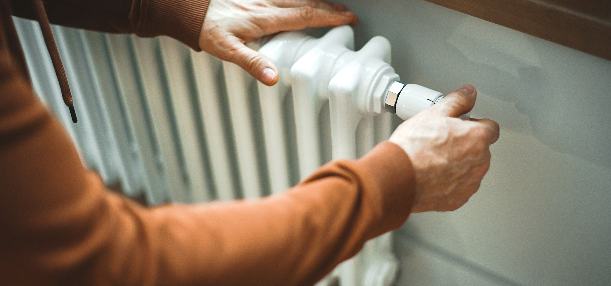 Eine Person stellt das Thermostat an einem Heizkörper ein.