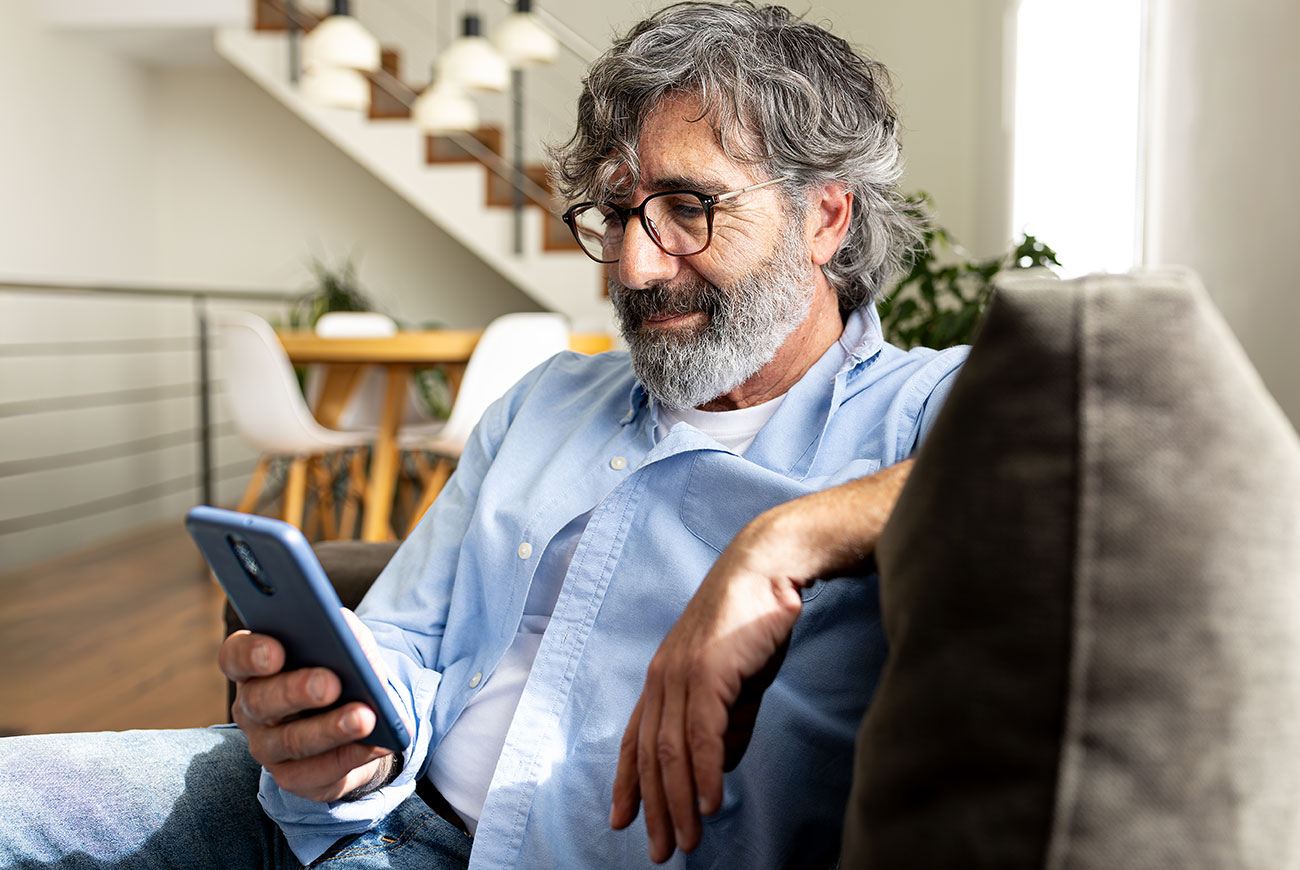 Ein Mann sitzt auf dem Sofa und schaut auf sein Smartphone.