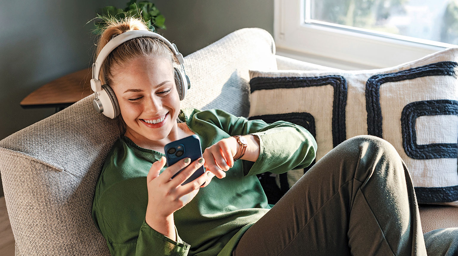 Frau entspannt sich auf dem Sofa mit Kopfhörern und Smartphone.