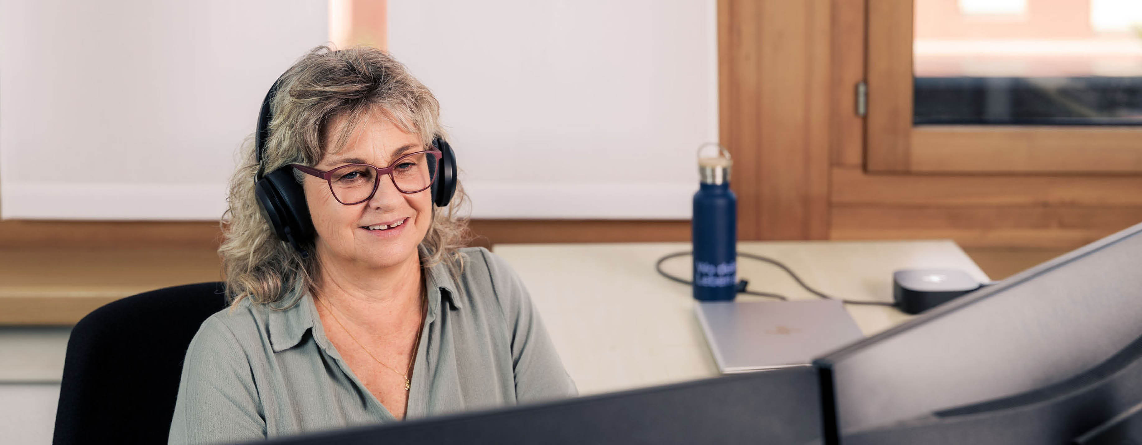 Mitarbeiterin im Kundendienst mit Headset vor dem Bildschirm.