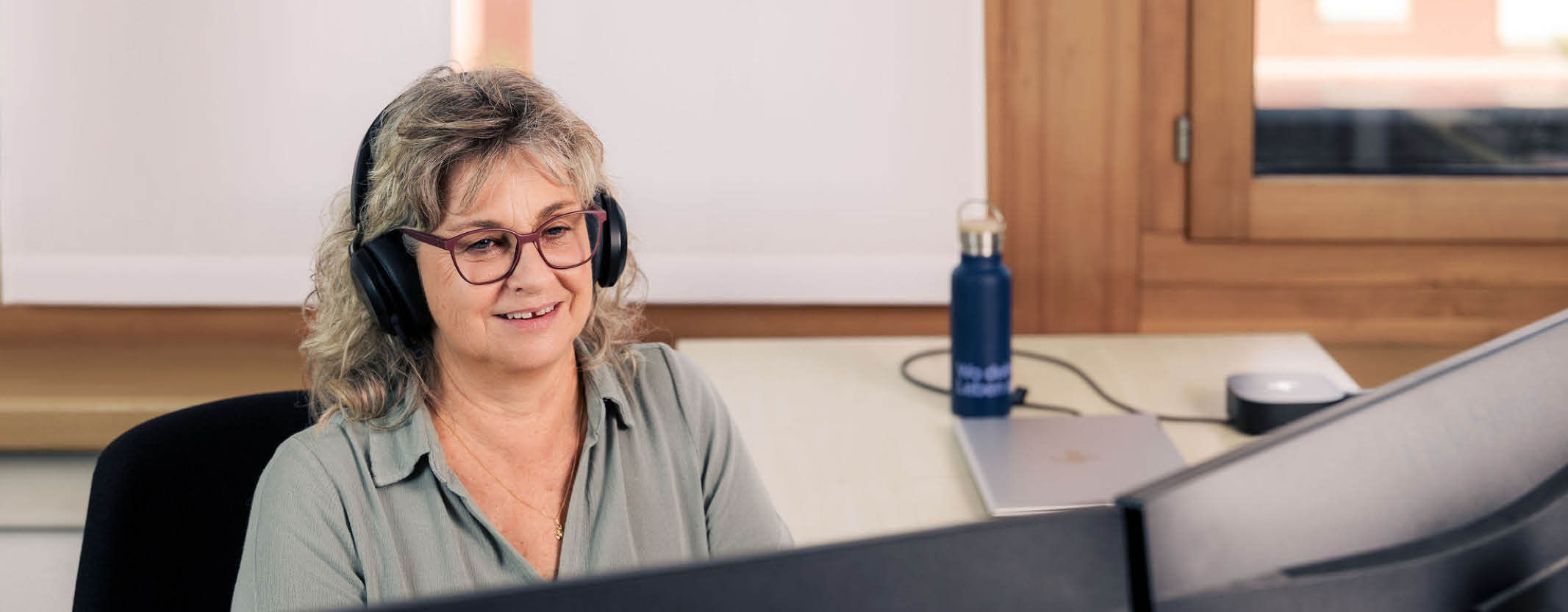 Mitarbeiterin im Kundendienst mit Headset vor dem Bildschirm.