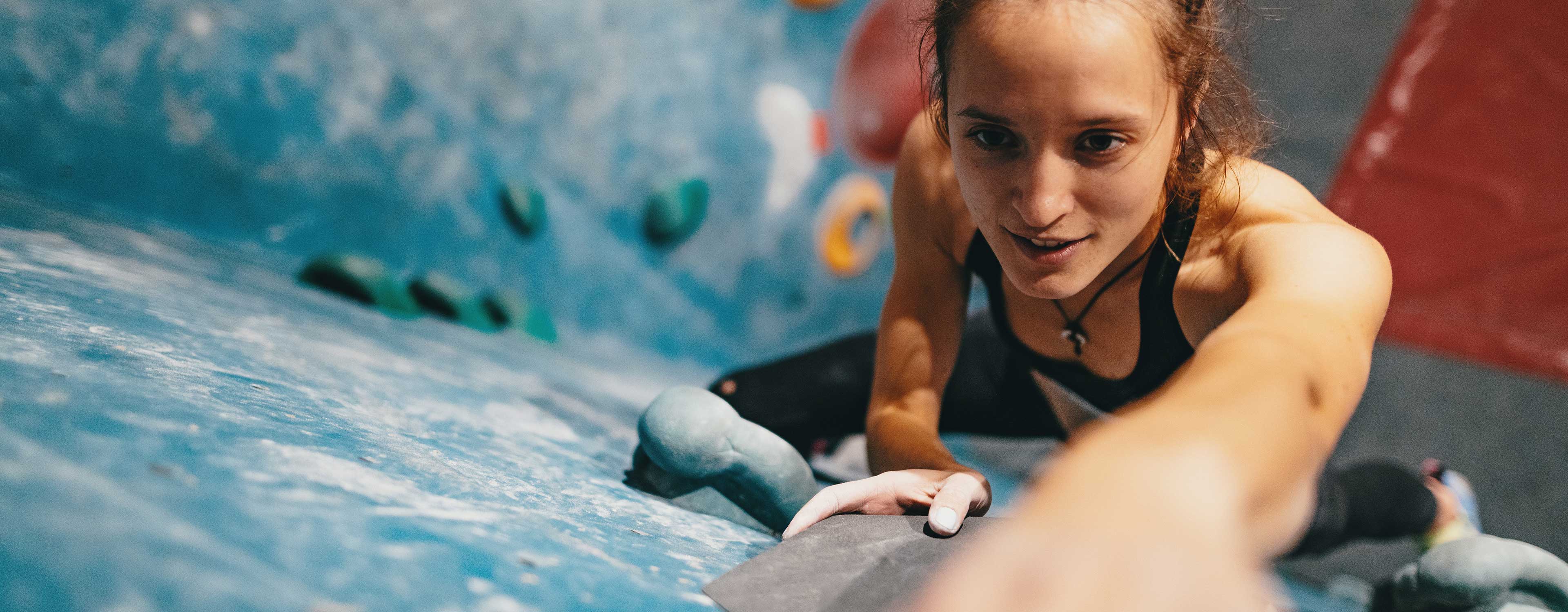 Junge Frau klettert konzentriert an einer bunten Boulderwand.