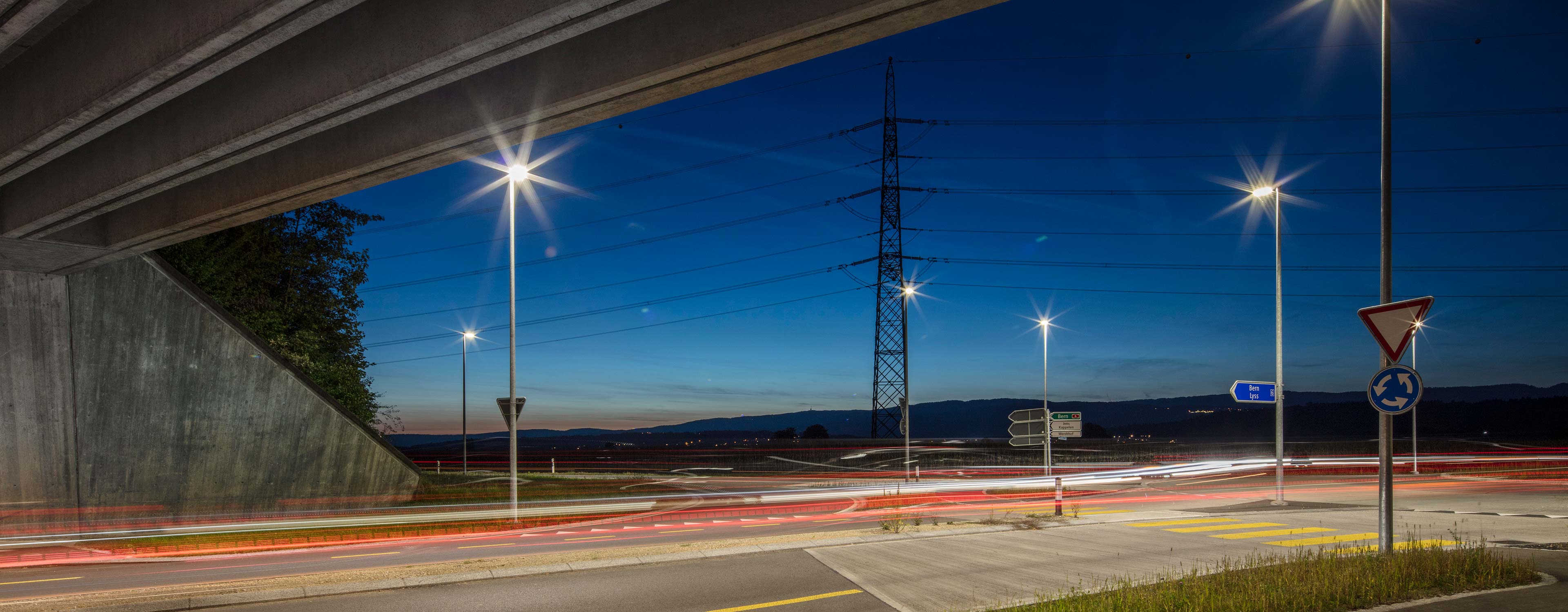 Beleuchteter Strassenkreisel in Lyss bei Nacht mit Blick auf Stromleitungen und den Jura.