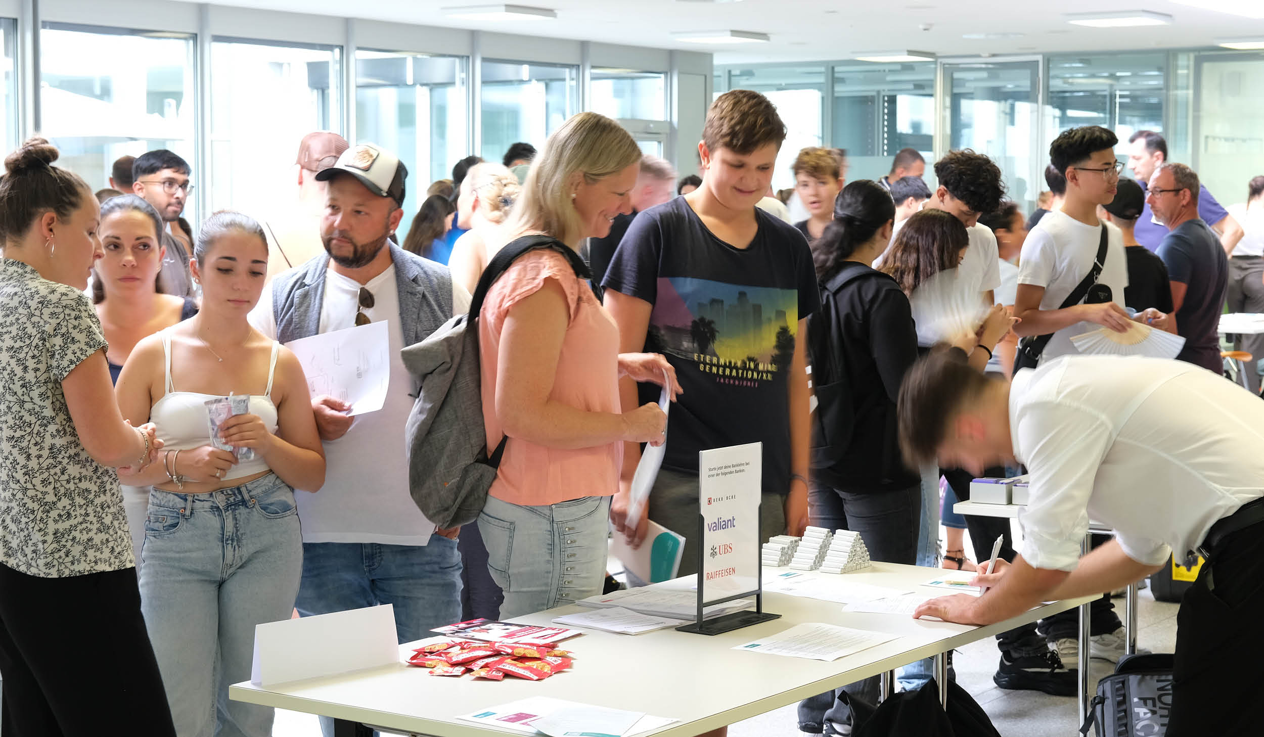 Besuchende im Gespräch an einem Stand der Lehrstellenbörse in einem Schulgebäude.