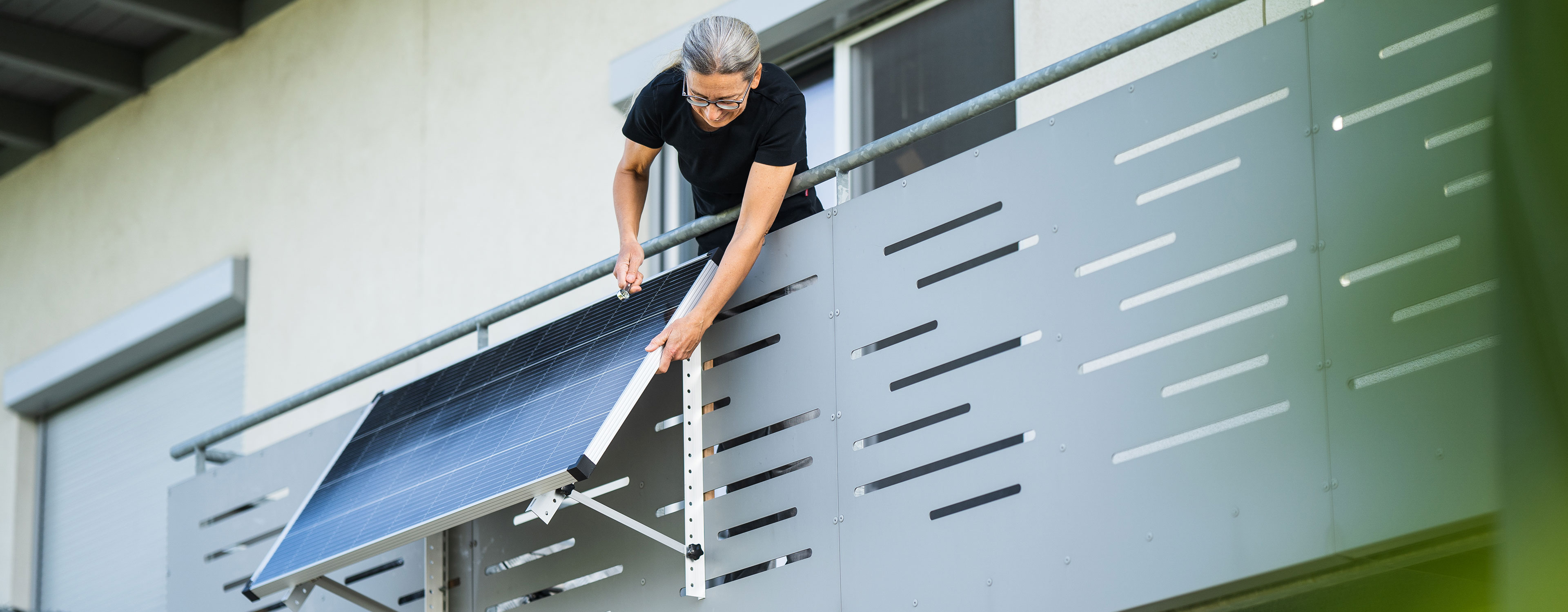Person montiert ein Balkonkraftwerk am Geländer ihres Wohnungsbalkons.