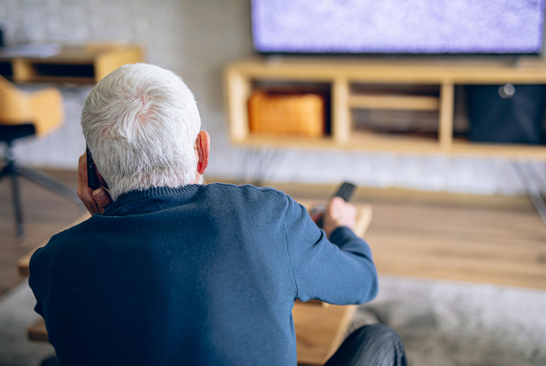 Ein älterer Mann telefoniert mit dem Kundendienst, während der Fernseher kein Signal zeigt.